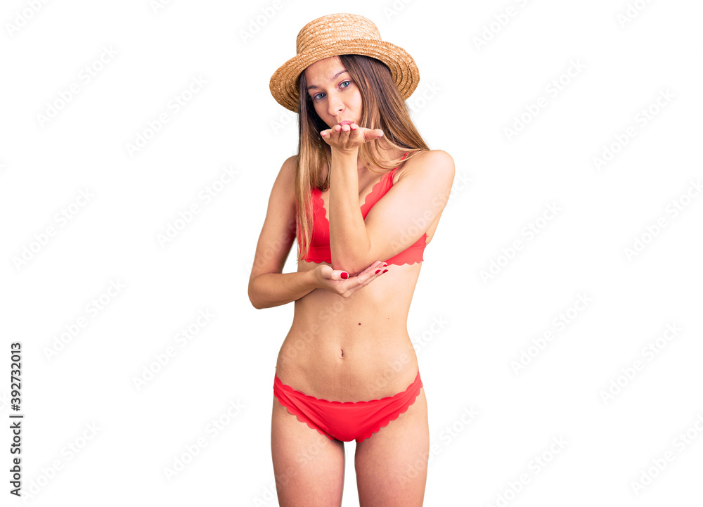 Beautiful brunette young woman wearing bikini looking at the camera blowing a kiss with hand on air being lovely and sexy. love expression. Beautiful brunette young woman wearing bikini looking at the camera blowing a kiss with hand on air being lovely and sexy. love expression.