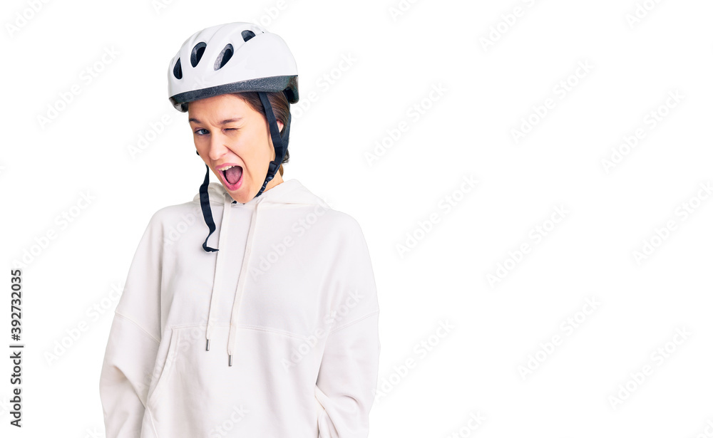 Beautiful brunette young woman wearing bike helmet and sporty clothes winking looking at the camera with sexy expression, cheerful and happy face. Beautiful brunette young woman wearing bike helmet and sporty clothes winking looking at the camera with sexy expression, cheerful and happy face.