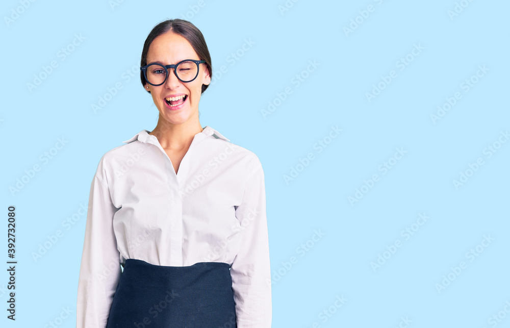Beautiful brunette young woman wearing professional waitress apron winking looking at the camera with sexy expression, cheerful and happy face. Beautiful brunette young woman wearing professional waitress apron winking looking at the camera with sexy expression, cheerful and happy face.