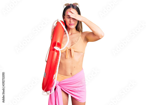 Beautiful brunette young woman wearing bikini and holding lifesaver float stressed and frustrated with hand on head, surprised and angry face