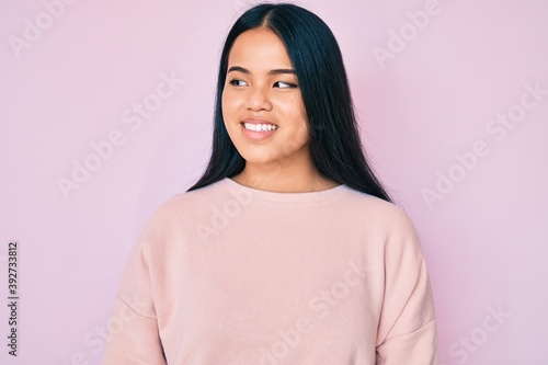 Young beautiful asian girl wearing casual pink sweater looking to side, relax profile pose with natural face and confident smile. © Krakenimages.com