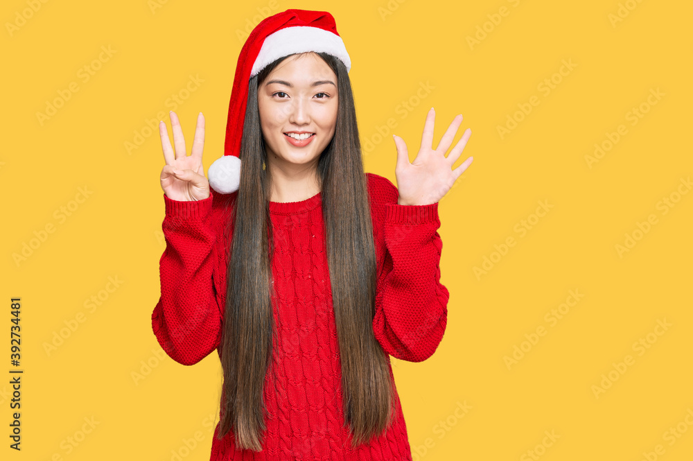 Young chinese woman wearing christmas hat showing and pointing up with fingers number eight while smiling confident and happy. Young chinese woman wearing christmas hat showing and pointing up with fingers number eight while smiling confident and happy.