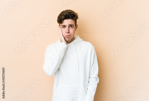Young caucasian man isolated on beige background blows cheeks, has tired expression. Facial expression concept.