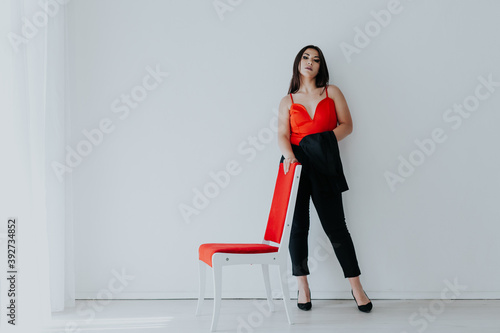 Beautiful brunette woman sits on a red chair in a white room