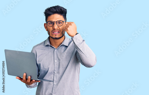 Handsome latin american young man working using computer laptop annoyed and frustrated shouting with anger, yelling crazy with anger and hand raised