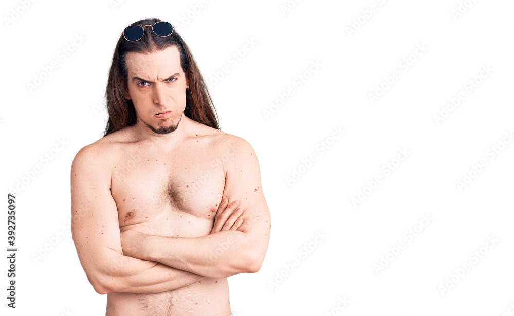 Young adult man with long hair wearing swimwear shirtless skeptic and nervous, disapproving expression on face with crossed arms. negative person. Young adult man with long hair wearing swimwear shirtless skeptic and nervous, disapproving expression on face with crossed arms. negative person.