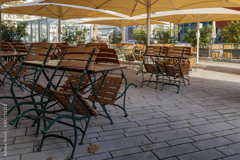 Selective focus at stack of outdoor chairs and tables of cafe on Schadowstraße, in Düsseldorf which closed during during epidemic of COVID-19 virus. COVID-19 restrictions on public cafe in Europe.