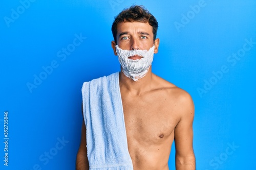 Handsome man saving beard with shave foam over face with serious expression on face. simple and natural looking at the camera.