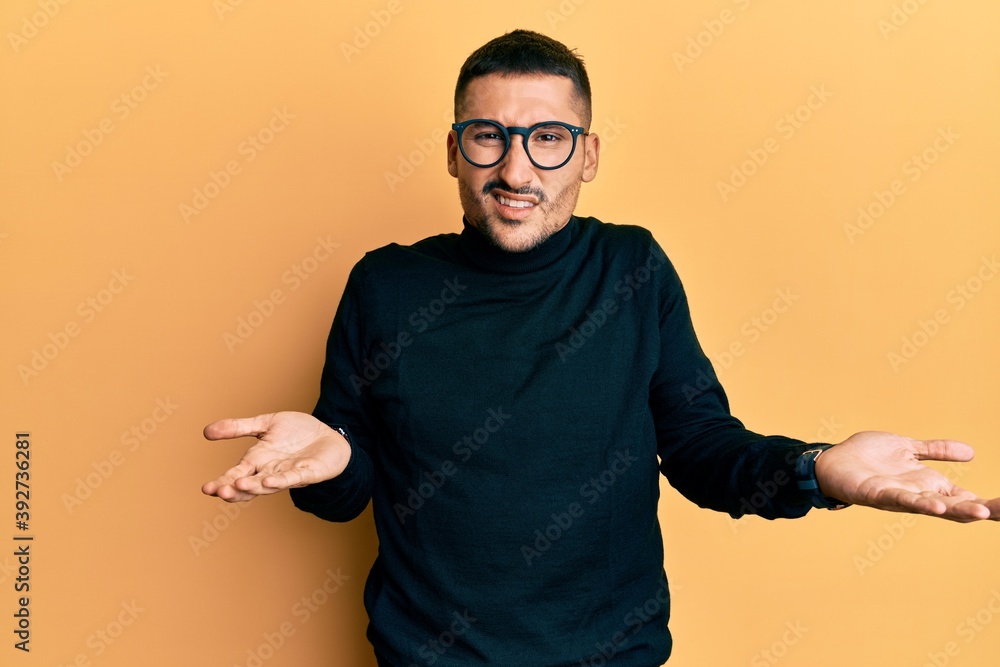 Handsome man with tattoos wearing turtleneck sweater and glasses clueless and confused with open arms, no idea concept. Handsome man with tattoos wearing turtleneck sweater and glasses clueless and confused with open arms, no idea concept.