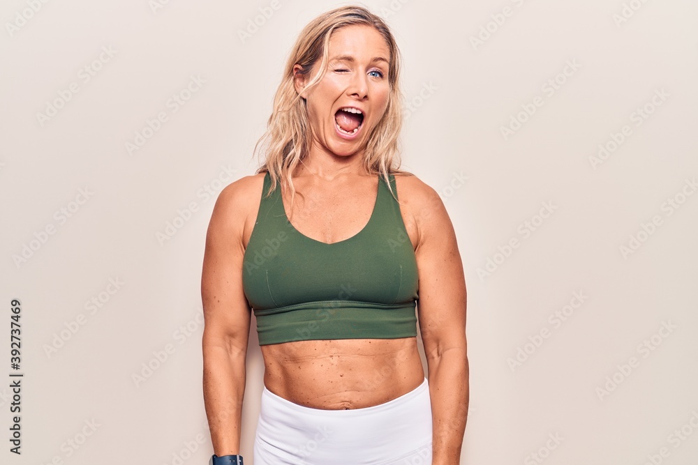 Middle age caucasian blonde woman wearing sportswear winking looking at the camera with sexy expression, cheerful and happy face. Middle age caucasian blonde woman wearing sportswear winking looking at the camera with sexy expression, cheerful and happy face.