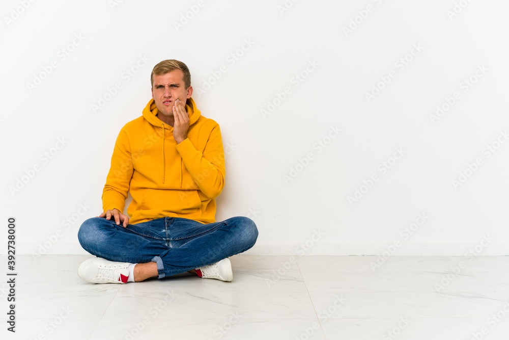 Young caucasian man sitting on the floor having a strong teeth pain, molar ache.