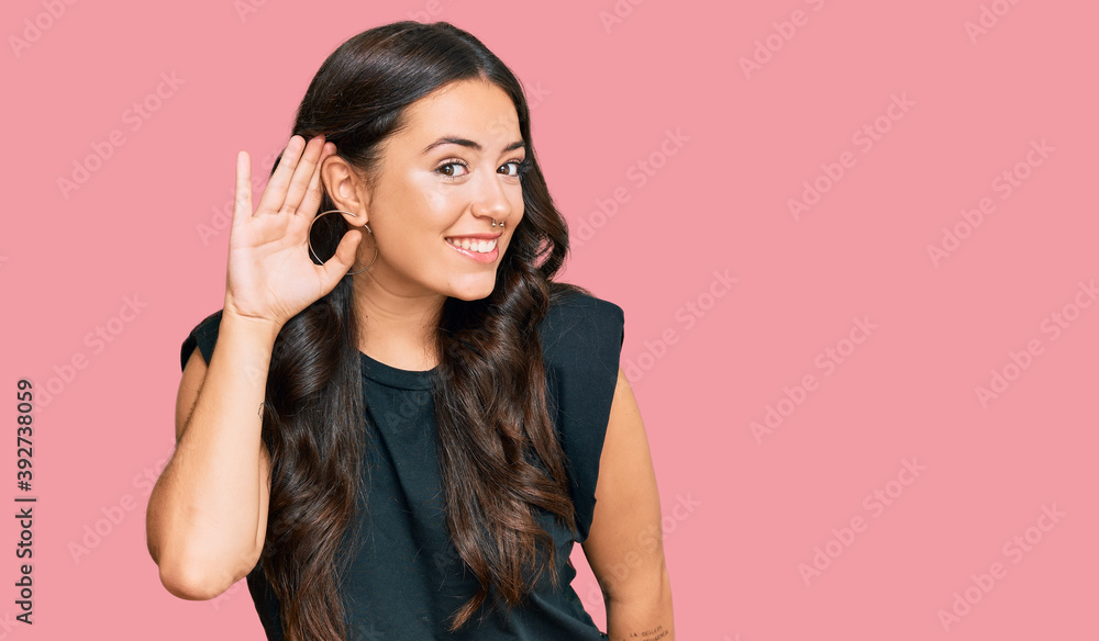 Beautiful brunette young woman wearing black shirt smiling with hand over ear listening an hearing to rumor or gossip. deafness concept. Beautiful brunette young woman wearing black shirt smiling with hand over ear listening an hearing to rumor or gossip. deafness concept.