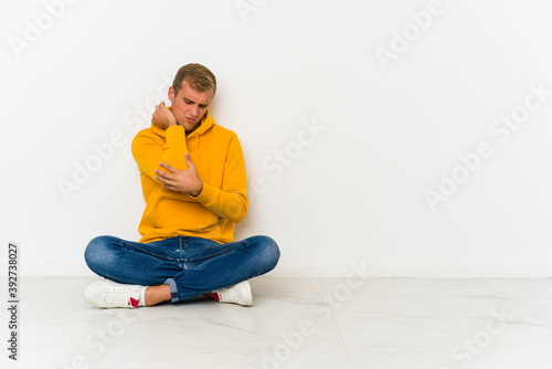 Young caucasian man sitting on the floor massaging elbow, suffering after a bad movement. © Asier