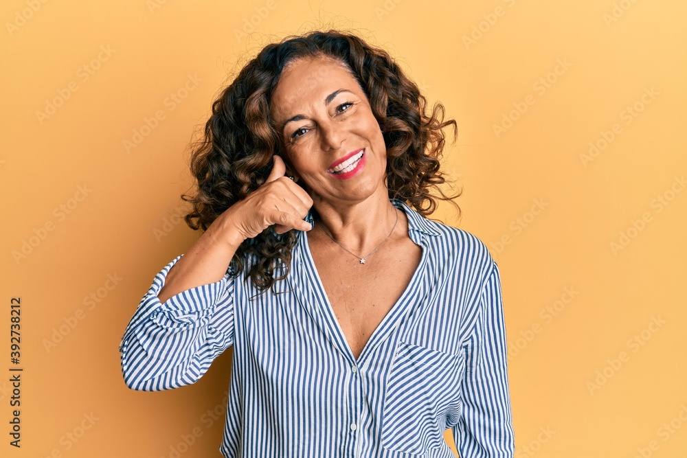Middle age hispanic woman wearing casual clothes smiling doing phone gesture with hand and fingers like talking on the telephone. communicating concepts. Middle age hispanic woman wearing casual clothes smiling doing phone gesture with hand and fingers like talking on the telephone. communicating concepts.