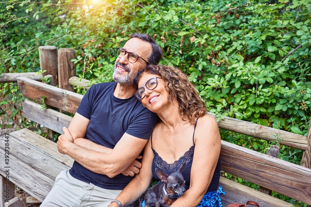 Middle age couple smiling happy looking at the sky. Sitting on the bench with chihuahua dog at park Middle age couple smiling happy looking at the sky. Sitting on the bench with chihuahua dog at park