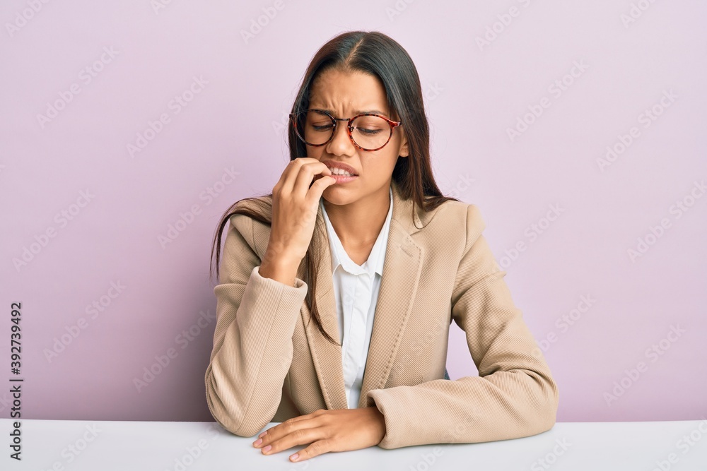 Beautiful hispanic woman working at the office looking stressed and nervous with hands on mouth biting nails. anxiety problem. Beautiful hispanic woman working at the office looking stressed and nervous with hands on mouth biting nails. anxiety problem.