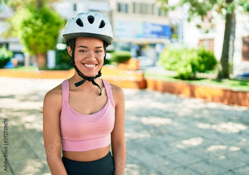 Young beautiful hispanic cyclist woman smiling happy wearing bike helmet at the town © Krakenimages.com