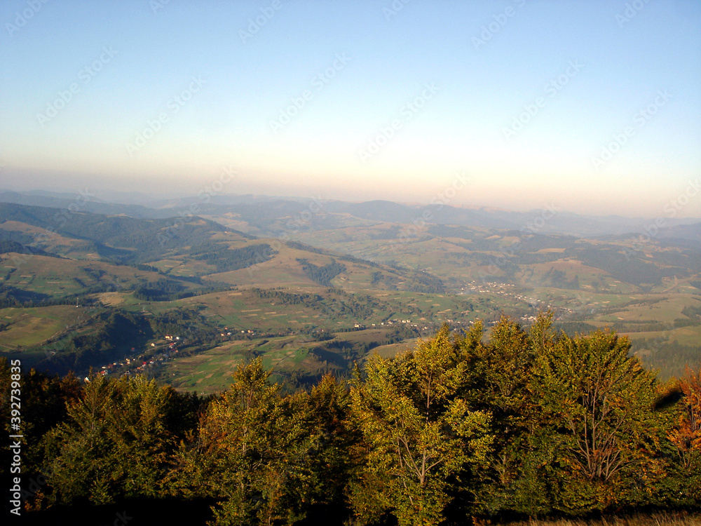Naklejka premium Trees in the foreground against the backdrop of a landscape of autumn mountains and highland valleys
