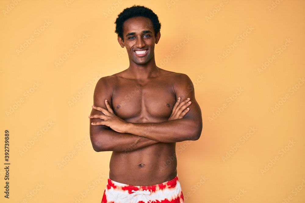 African handsome man wearing swimsuit happy face smiling with crossed arms looking at the camera. positive person.