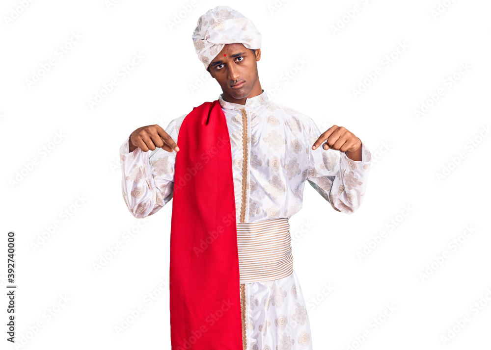 African handsome man wearing tradition sherwani saree clothes pointing down looking sad and upset, indicating direction with fingers, unhappy and depressed. African handsome man wearing tradition sherwani saree clothes pointing down looking sad and upset, indicating direction with fingers, unhappy and depressed.