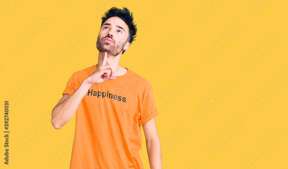 Young hispanic man wearing t shirt with happiness word message thinking concentrated about doubt with finger on chin and looking up wondering Young hispanic man wearing t shirt with happiness word message thinking concentrated about doubt with finger on chin and looking up wondering