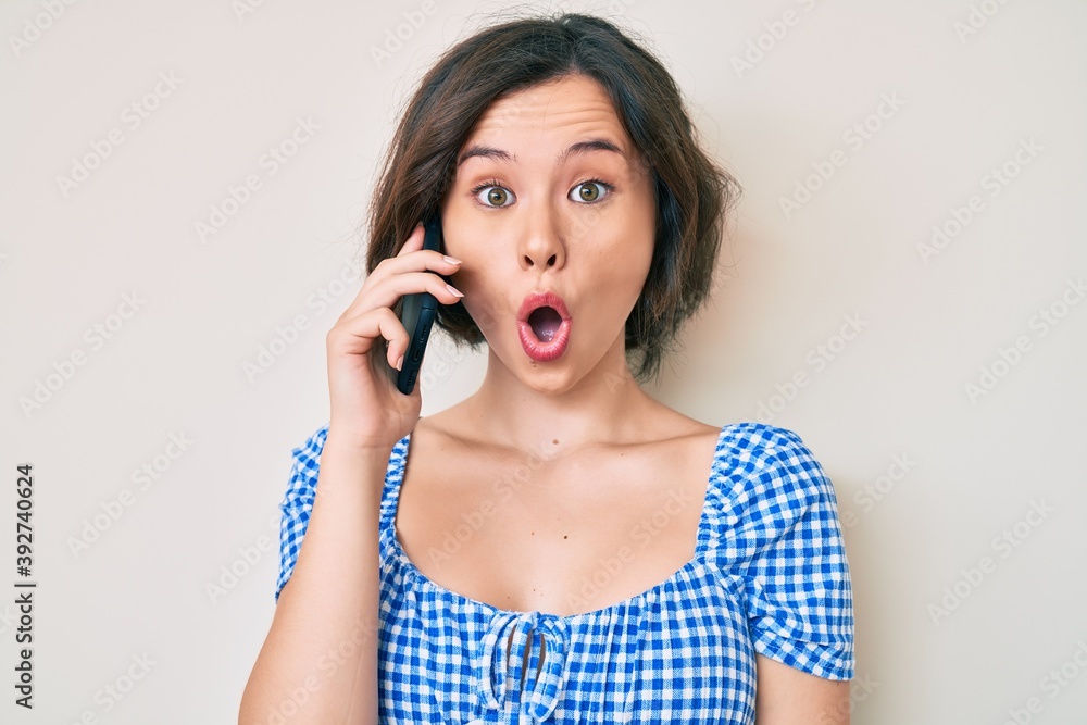 Young beautiful girl having conversation talking on the smartphone scared and amazed with open mouth for surprise, disbelief face Young beautiful girl having conversation talking on the smartphone scared and amazed with open mouth for surprise, disbelief face