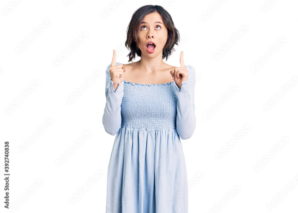 Young beautiful girl wearing casual clothes amazed and surprised looking up and pointing with fingers and raised arms. Young beautiful girl wearing casual clothes amazed and surprised looking up and pointing with fingers and raised arms.