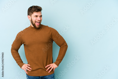 Young caucasian man isolated on blue background laughs and closes eyes, feels relaxed and happy.