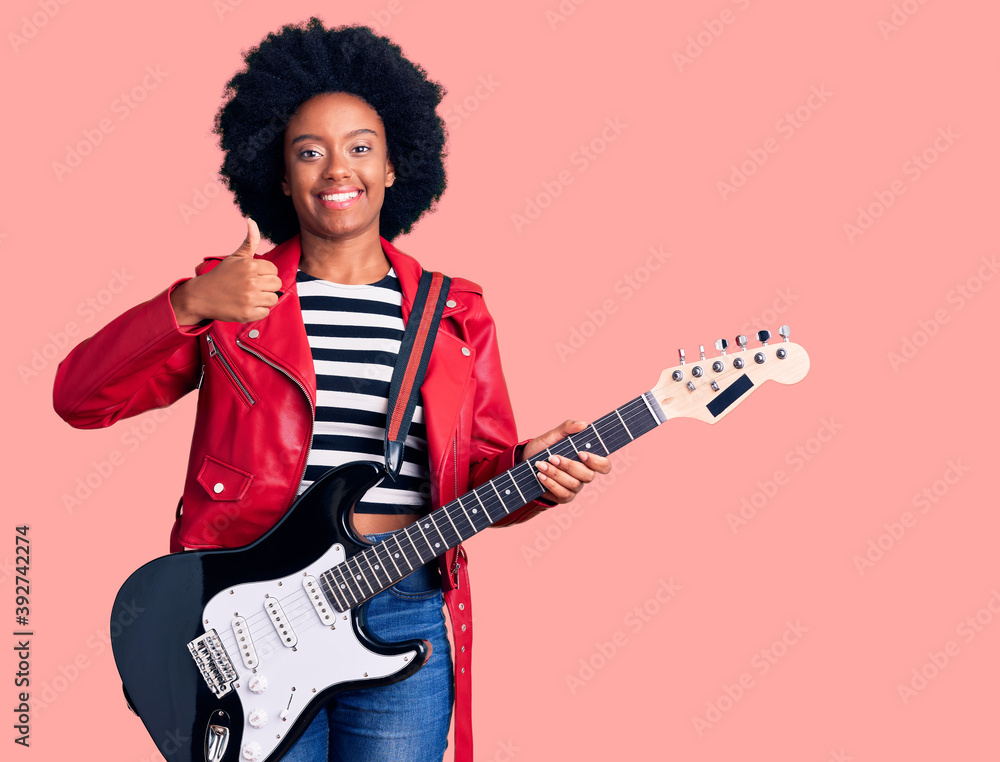 Obraz premium Young african american woman playing electric guitar smiling happy and positive, thumb up doing excellent and approval sign