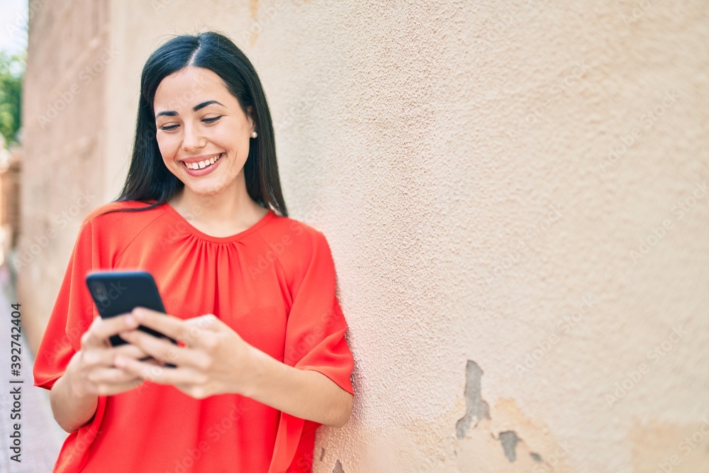 Fototapeta premium Young latin girl smiling happy using smartphone at the city.