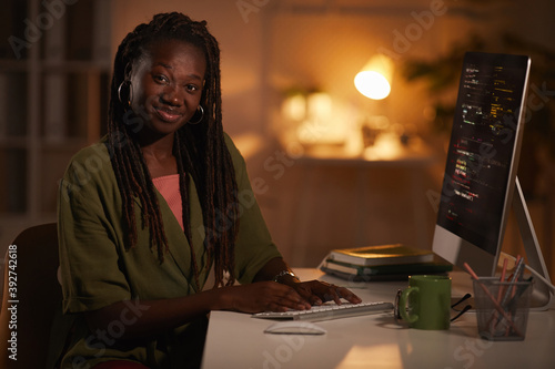 Portrait of contemporary African-American woman writing code and looking at camera while working in dark office, copy space photo