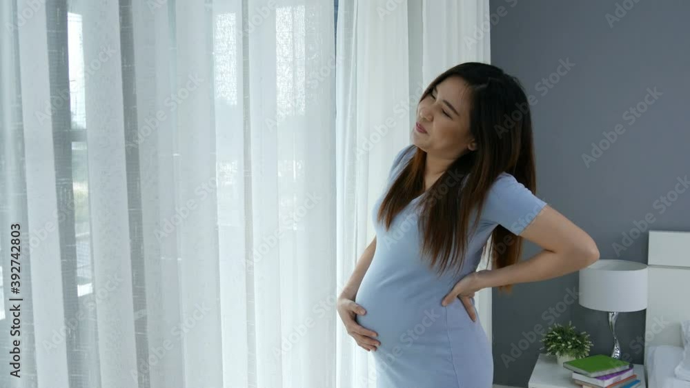Pregnant woman suffering lower back pain in a bedroom Pregnant woman suffering lower back pain in a bedroom