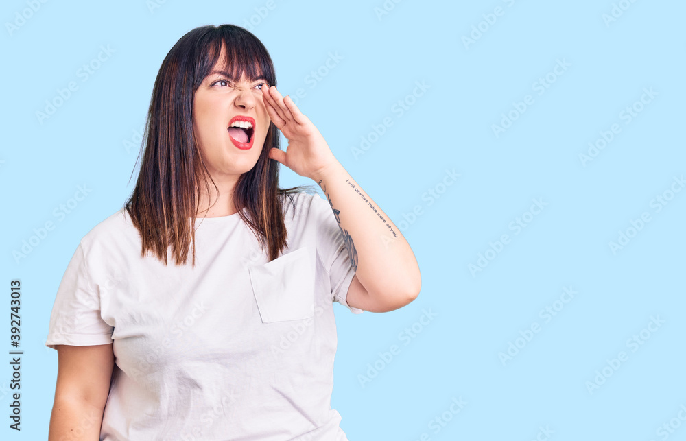 Young plus size woman wearing casual clothes shouting and screaming loud to side with hand on mouth. communication concept. Young plus size woman wearing casual clothes shouting and screaming loud to side with hand on mouth. communication concept.