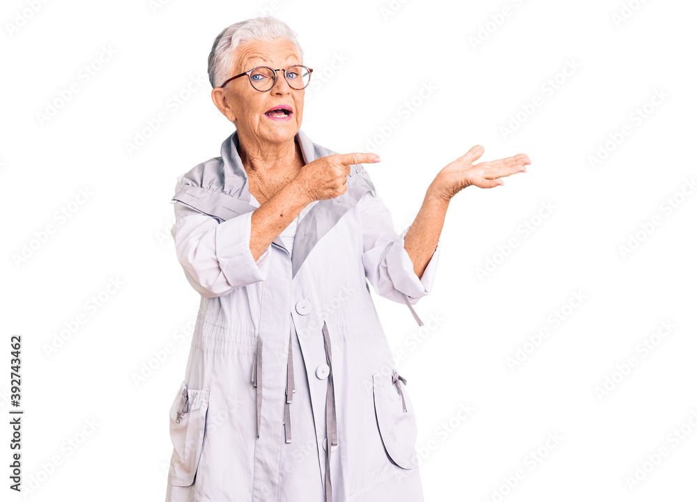 Senior beautiful woman with blue eyes and grey hair wearing casual clothes and glasses amazed and smiling to the camera while presenting with hand and pointing with finger. Senior beautiful woman with blue eyes and grey hair wearing casual clothes and glasses amazed and smiling to the camera while presenting with hand and pointing with finger.