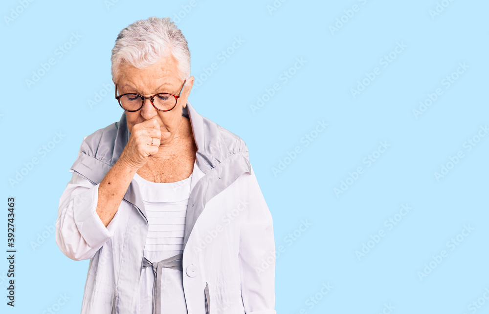 Senior beautiful woman with blue eyes and grey hair wearing casual clothes and glasses feeling unwell and coughing as symptom for cold or bronchitis. health care concept. Senior beautiful woman with blue eyes and grey hair wearing casual clothes and glasses feeling unwell and coughing as symptom for cold or bronchitis. health care concept.