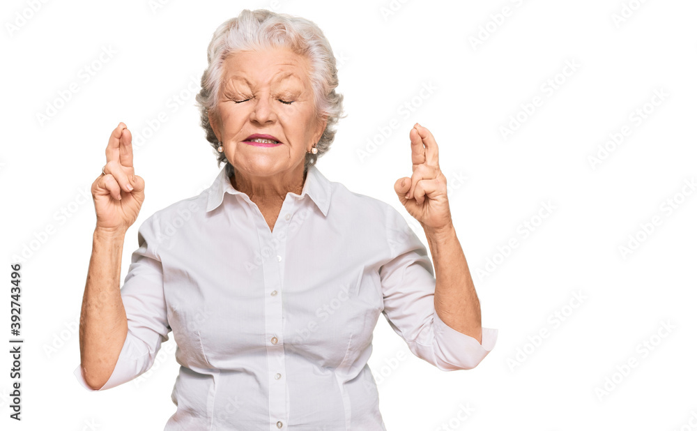 Senior grey-haired woman wearing casual clothes gesturing finger crossed smiling with hope and eyes closed. luck and superstitious concept. Senior grey-haired woman wearing casual clothes gesturing finger crossed smiling with hope and eyes closed. luck and superstitious concept.