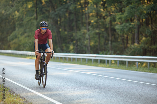 Fototapeta Naklejka Na Ścianę i Meble -  Cyclist riding bike on asphalt road among nature