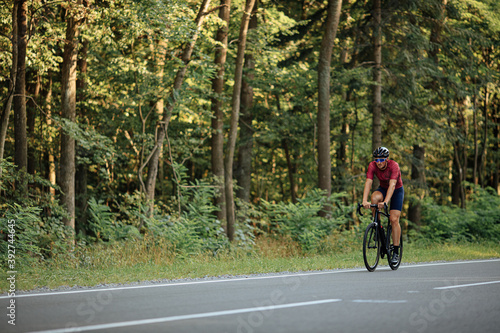 Fototapeta Naklejka Na Ścianę i Meble -  Young sportsman riding bike among green forest