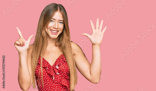 Beautiful blonde woman wearing summer dress showing and pointing up with fingers number seven while smiling confident and happy.