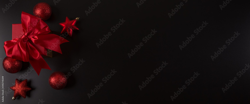 Gift with a bow, red Christmas balls on a black background. New Year Christmas texture, backdrop, design idea. Web banner Gift with a bow, red Christmas balls on a black background. New Year Christmas texture, backdrop, design idea. Web banner