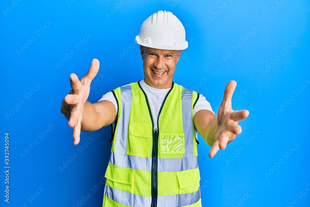 Middle age bald man wearing architect hardhat looking at the camera smiling with open arms for hug. cheerful expression embracing happiness. Middle age bald man wearing architect hardhat looking at the camera smiling with open arms for hug. cheerful expression embracing happiness.