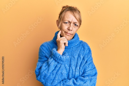 Middle age blonde woman wearing casual winter sweater thinking concentrated about doubt with finger on chin and looking up wondering