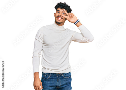 Young arab man wearing casual winter sweater doing peace symbol with fingers over face, smiling cheerful showing victory