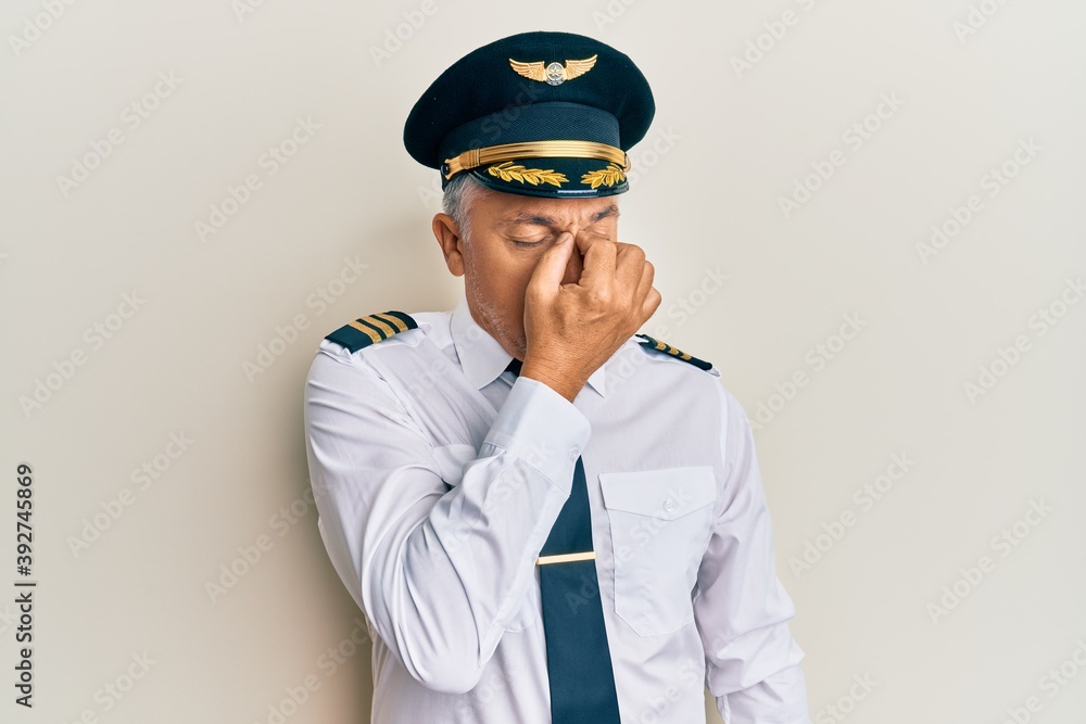 Handsome middle age mature man wearing airplane pilot uniform tired rubbing nose and eyes feeling fatigue and headache. stress and frustration concept. Handsome middle age mature man wearing airplane pilot uniform tired rubbing nose and eyes feeling fatigue and headache. stress and frustration concept.