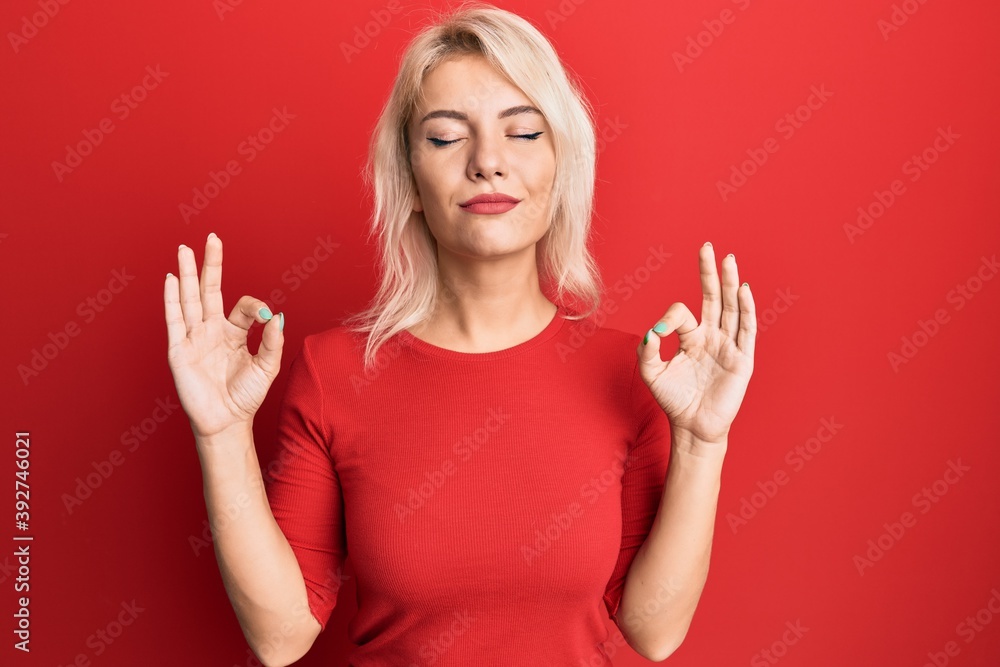 Young blonde girl wearing casual clothes relax and smiling with eyes closed doing meditation gesture with fingers. yoga concept. Young blonde girl wearing casual clothes relax and smiling with eyes closed doing meditation gesture with fingers. yoga concept.