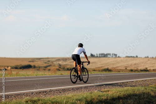 Back view of young man in helmet riding bike on road