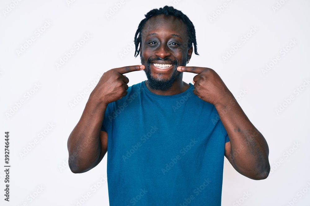 Fototapeta premium Young african american man with braids wearing casual clothes smiling cheerful showing and pointing with fingers teeth and mouth. dental health concept.
