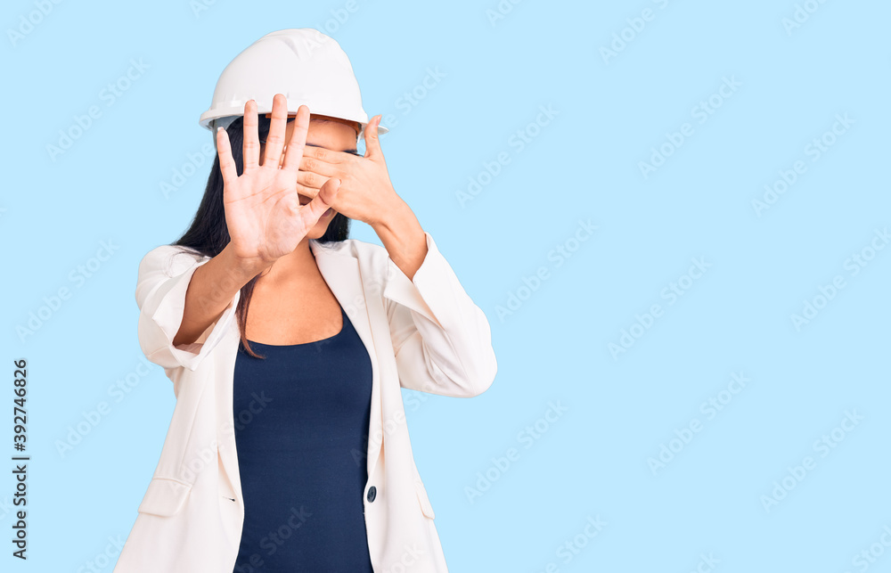Young beautiful latin girl wearing architect hardhat and glasses covering eyes with hands and doing stop gesture with sad and fear expression. embarrassed and negative concept. Young beautiful latin girl wearing architect hardhat and glasses covering eyes with hands and doing stop gesture with sad and fear expression. embarrassed and negative concept.