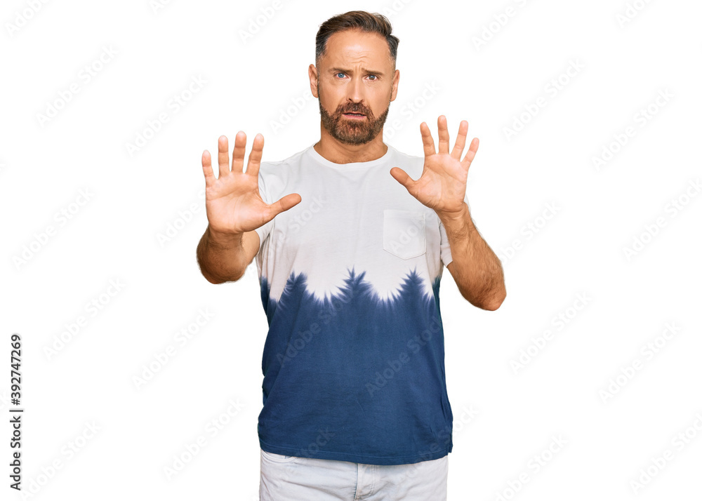 Handsome middle age man wearing casual tie dye tshirt afraid and terrified with fear expression stop gesture with hands, shouting in shock. panic concept. Handsome middle age man wearing casual tie dye tshirt afraid and terrified with fear expression stop gesture with hands, shouting in shock. panic concept.