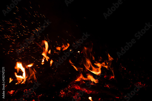 Burning red hot sparks rise from large fire in the night. Fire flames sparks background. Abstract dark glitter fire particles lights.